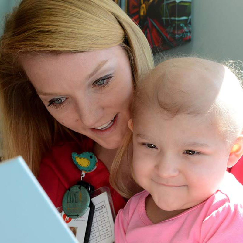 HDFS alum & Child Life specialist Lindsey Smith reading a book with a child at Childen's of Alabama.