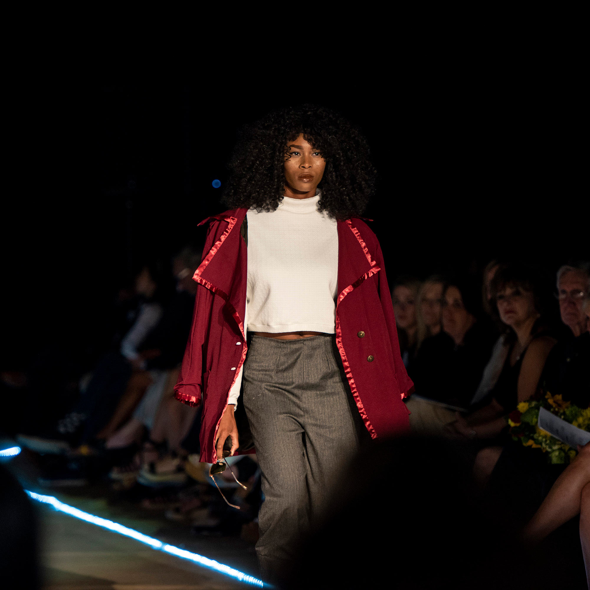 Model walking the runway in a marron coat and grey pants during The Fashion Event: Mod.