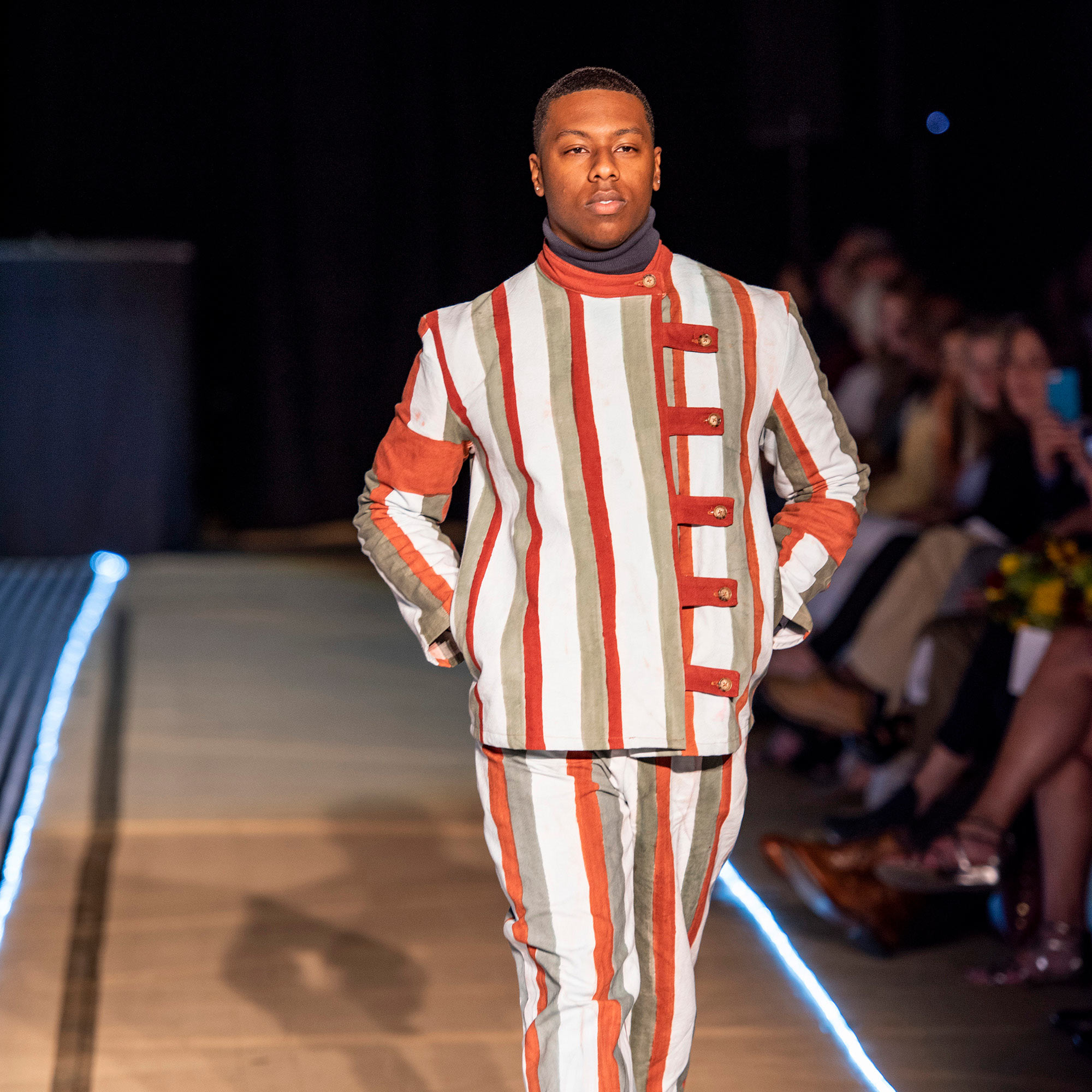 Model walking the runway in a grey, red and white striped jacket and pants during The Fashion Event: Mod.