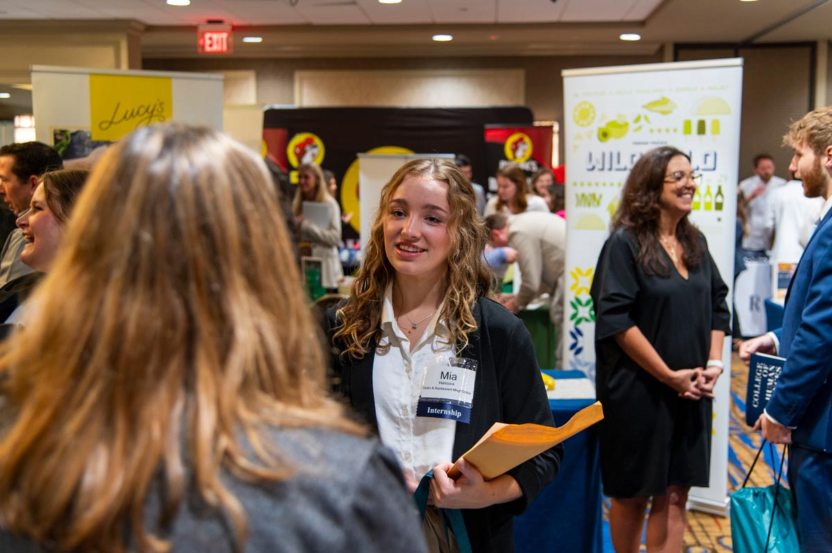 Female student in pink blazer looking at a vendor table.