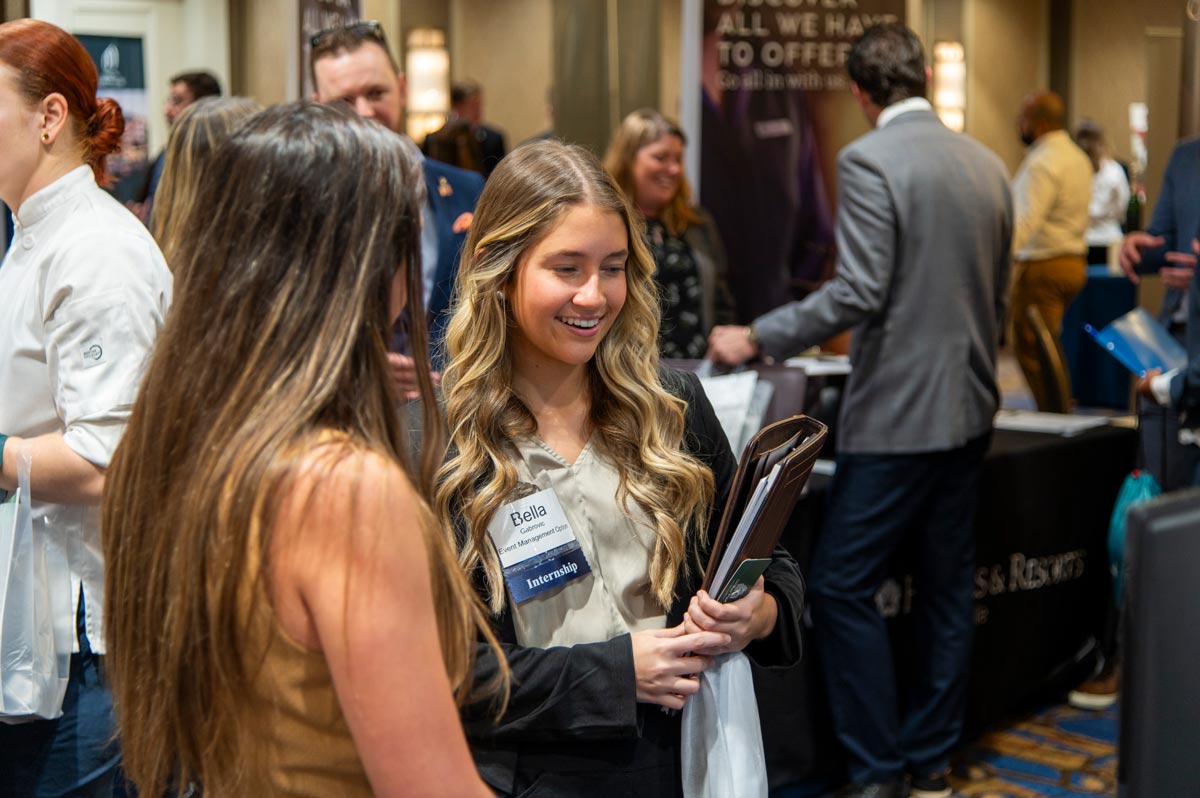 Two Hosp students smiling while talking to vendor at the career fair.